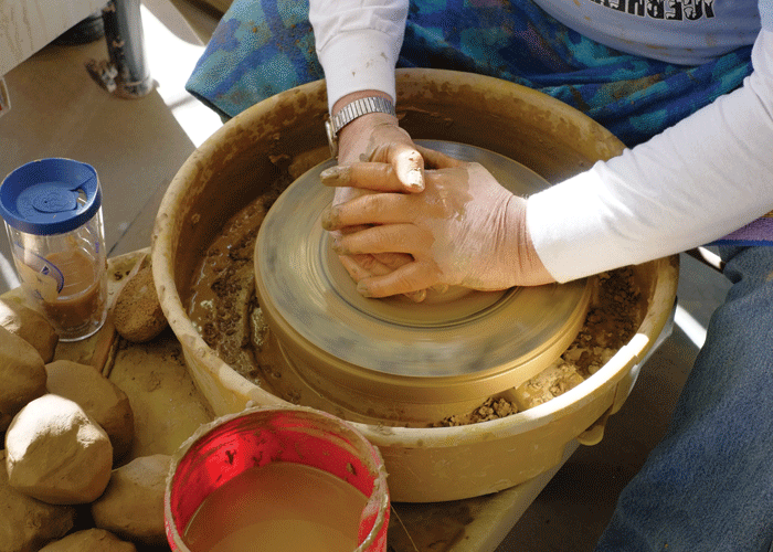 Hands forming clay on a pottery wheel